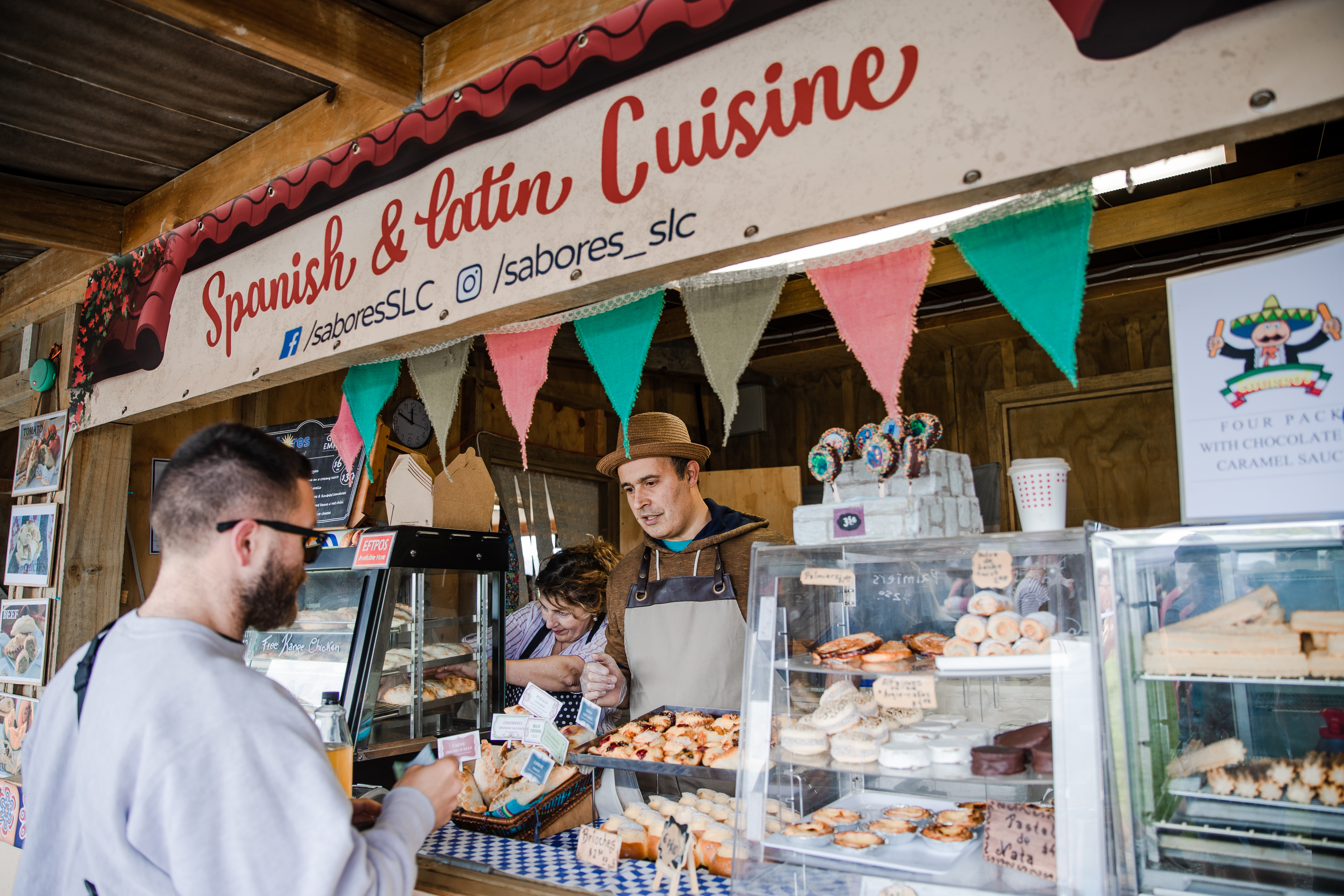 Man in a grey jumper ordering at a Spanish food vendor at Clevedon Market in Auckland