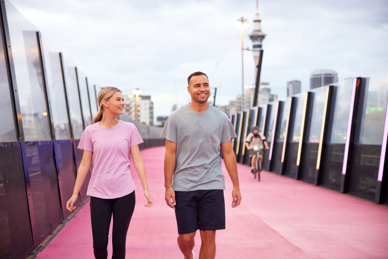 Two people walk along The pink path with Auckland city in background