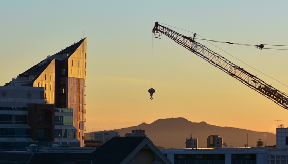 Silhouette of crane and building in Auckland at sunset with Rangitoto Island in background.
