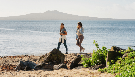 Two girls walking on a beach in Auckland with a view of Rangitoto